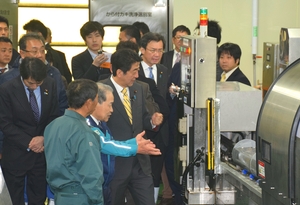 かき超高圧処理装置の説明を受ける首相(中央)